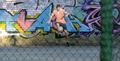Young Adult Juggling Soccer Ball Against Graffiti Wall