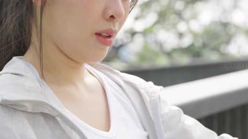 4K Asian woman drinking water from a bottle while jogging at public park in the morning.