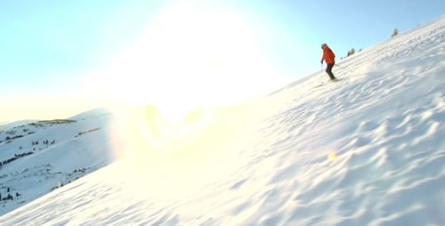 Person Skiing Down Snowy Mountain Slope on Sunny Day