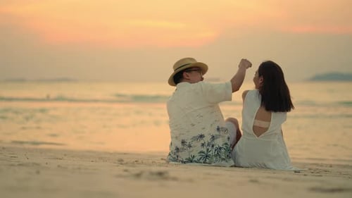 4K Happy Asian couple sitting and embracing each other on tropical island beach at summer sunset