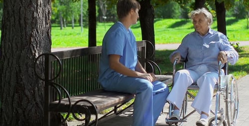 Young Aide with Senior Woman in Wheelchair in Park