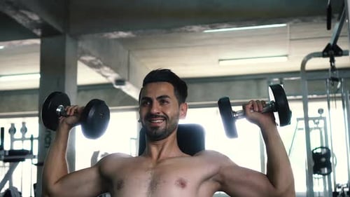 Muskulöser, kräftiger junger Mann beim Drücken der Schultern über dem Kopf mit Hanteln im Fitnessstudio