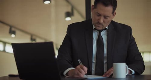 A man in a formal suit working at the office, signing documents. Mediums shot, slow motion.