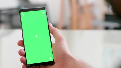 Close-up Shot of a Smartphone with Green Screen on in Man's Hand