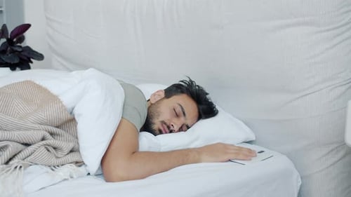 Un beau mec arabe se réveille en regardant l'écran d'un smartphone puis dormant à nouveau dans son lit à la maison