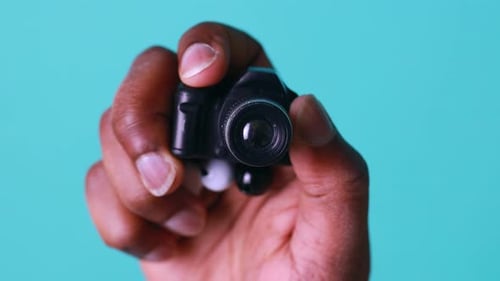 Mini Camera in Hand of African American Man in Blue Studio