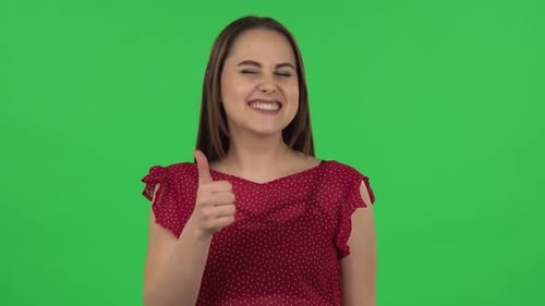 Porträt eines zarten Mädchens im roten Kleid zeigt Daumen hoch, gestenartig. Greenscreen