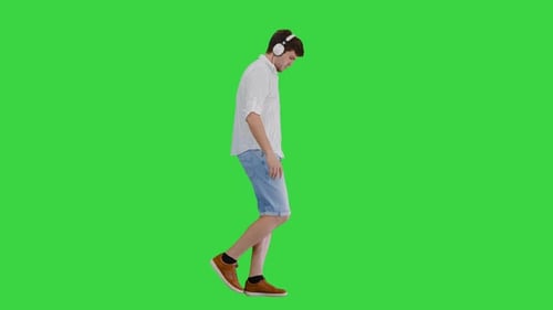 Casual Young Man Listening To Music in Headphones While Walking on a Green Screen Chroma Key