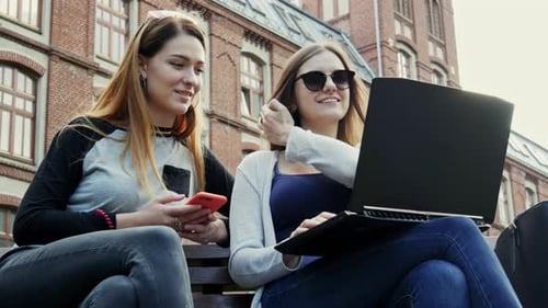 Two Young Women Using Laptop on Park Bench