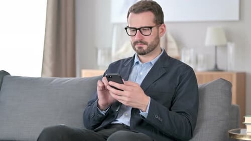 Man Sitting on Couch Looking at Phone