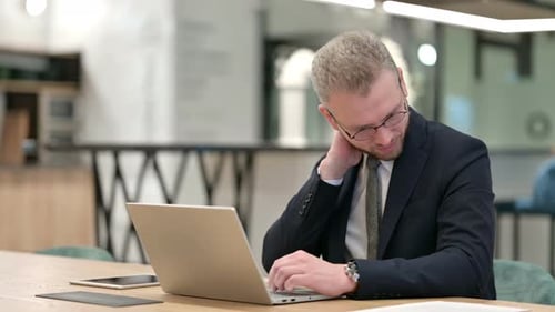 Tired Businessman with Laptop Having Neck Pain in Office