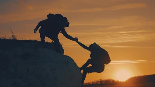 Silhouette of Helping Hand Between Two Climber. Two Hikers on Top of the Mountain, a Man Helps a