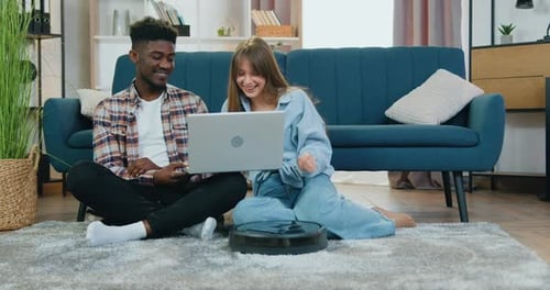 Pareja multiétnica que ve un Vídeo interesante en una computadora portátil en el suelo