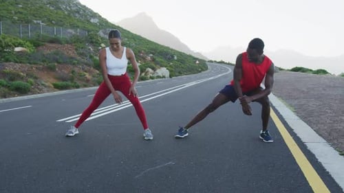 Diverse fit couple exercising stretching on a country road near mountains