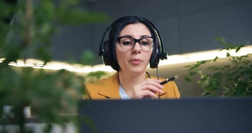 Mujer con ropa elegante con auriculares sentada frente a una computadora portátil durante un seminario web en línea