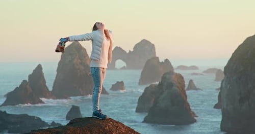 Woman Standing on Rocky Coast at Sunset