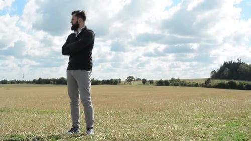 Junger gutaussehender Hipster-Mann steht im Feld und schaut sich um - Bewölkter Himmel