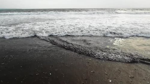 Pull back shot at the beach, as the ocean is full with trash, waves washing out plastic to the shore