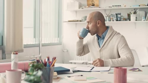 Man Drinking Coffee and Smiling at Desk in Office