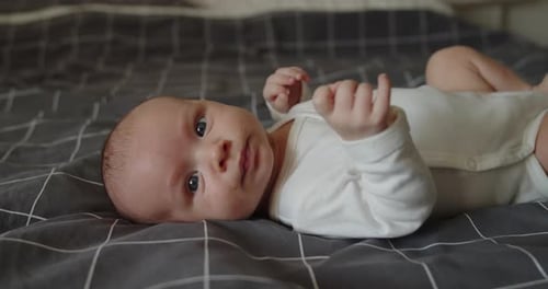 Adorable Infant Lying on Bed Waving Arms