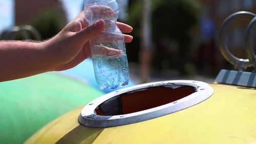 Hand Discards Plastic Bottle Into Yellow Recycling Container