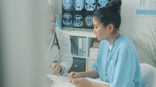 Doctor and Nurse Using Tablet Touching Screen and Talking Working in Hospital Office