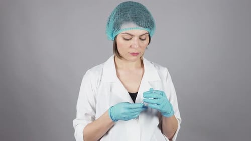Junge Ärztin in Handschuhen hält eine Spritze und bereitet die Injektion vor, isoliert auf grauem Hintergrund
