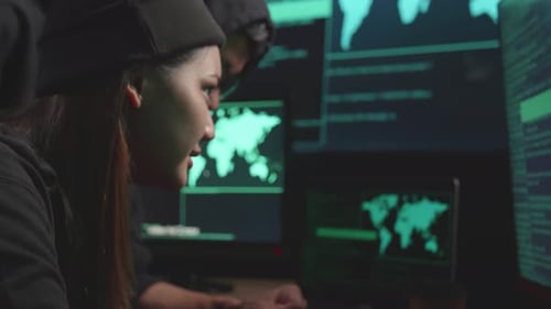 Un jeune couple asiatique de pirates informatiques utilise le piratage informatique et code sur plusieurs écrans d'ordinateur