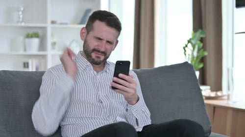 Man Upset While Looking at Smartphone on Sofa