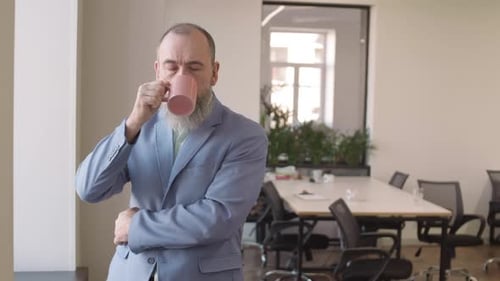 Man in Suit Drinks From Mug in Office