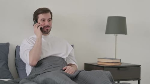 Jeune homme parlant sur appel sur smartphone au lit
