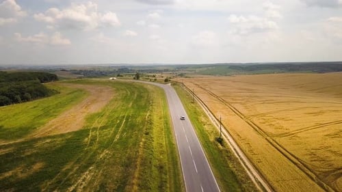 Aerial view of a road with moving cars between yellow agriculture wheat fields ready