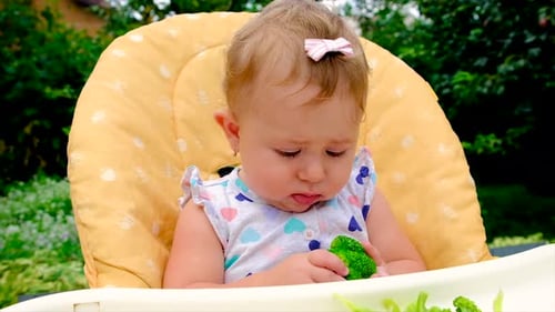 Adorable Baby Holding Broccoli in Highchair Outdoors