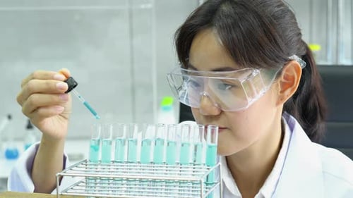 Woman Scientist Adds Blue Solution to Test Tubes