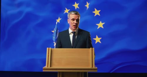 Man Speaks at Podium Before EU Flag