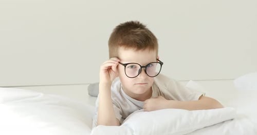 Smiling Boy Lying on Bed Playing With Glasses