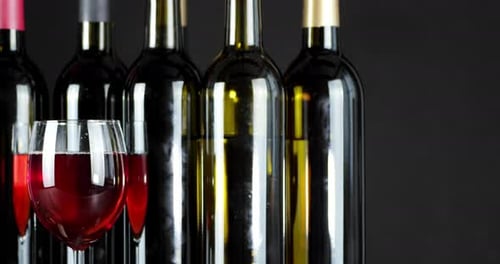 Ein Glas Rotwein und Flaschen drehen sich langsam. Auf einem schwarzen Hintergrund.