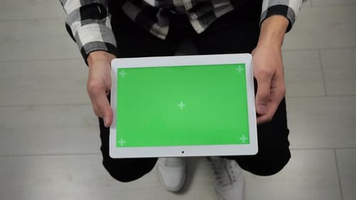 Mann sitzt auf Stuhl und blickt auf digitales Tablet mit Greenscreen-Chroma-Key