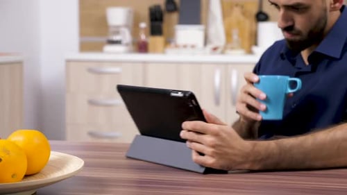 Man Using Tablet in Kitchen Sipping Drink