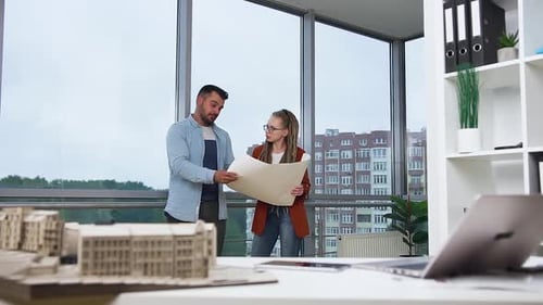 Man and Woman with Dreadlocks Standing in Design Office and Discussing Blueprint
