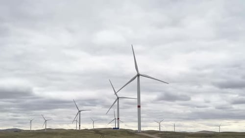 Bewegen Sie die Blätter einer großen Windkraftanlage in einem Feld vor dem Hintergrund eines bewölkten grauen Himmels auf dem