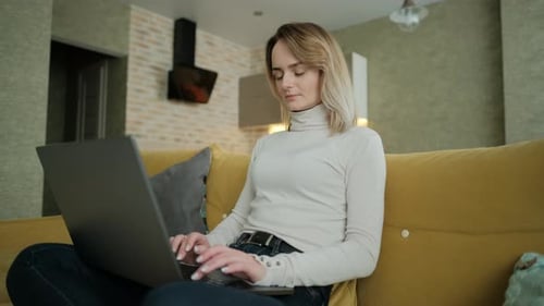 Young Adult Woman Typing on Laptop on Yellow Couch