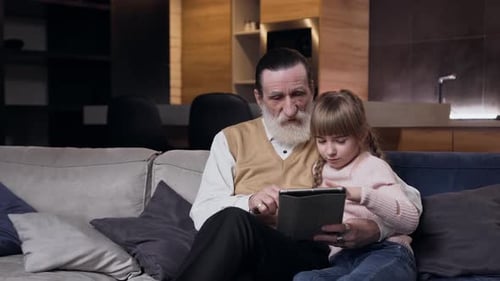 Grandfather and Granddaughter Enjoying Tablet Time on Couch