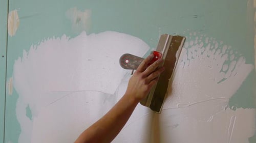 Woman Smoothing Plaster on Wall with Trowel