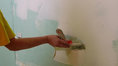 Person Applies Spackle to Drywall Wall