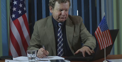 Man Writes at Desk With American Flag