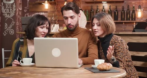Three Adults At Cafe Table Looking At Laptop