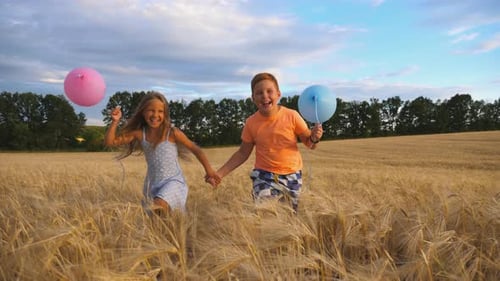 Couple of Happy Little Kids with Balloons in Arms Jogging Through Wheat Field. Small Girl and Boy