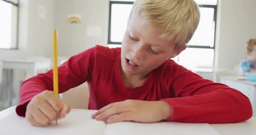 Video of happy caucasian boy sitting at school desk and writing