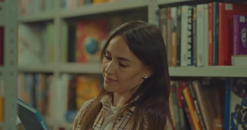 Porträt einer schönen Frau nimmt ein interessantes Buch aus dem Regal und beginnt es anzusehen